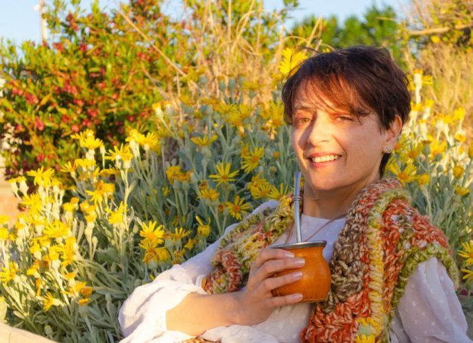 A woman smiles while drinking traditional mate among yellow flowers in Montevideo.
