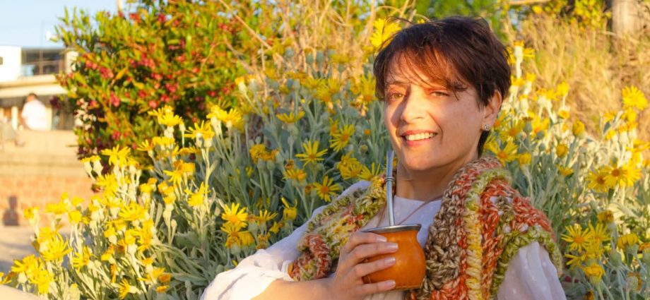 A woman smiles while drinking traditional mate among yellow flowers in Montevideo.