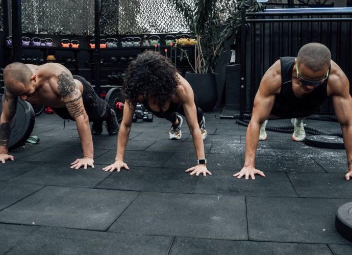 Three individuals performing push-ups together in a Mexico City gym setting.